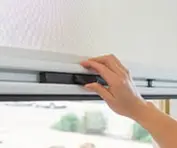Hand adjusting a window blind mechanism.